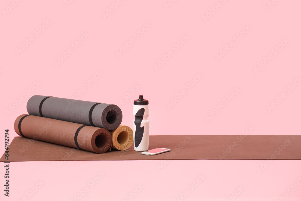 Fitness mats with bottle and mobile phone on pink background