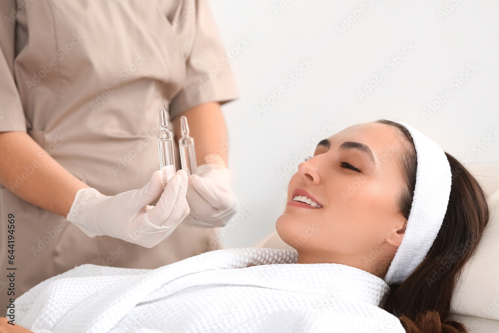 Beautiful young woman and cosmetologist with ampules in beauty salon, closeup