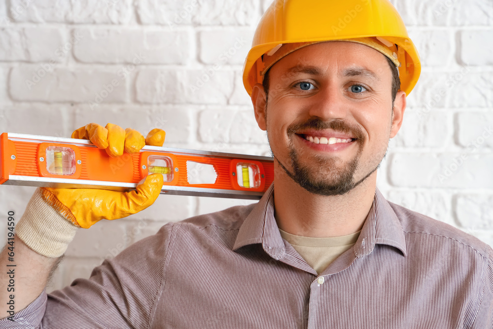 Male builder with level near white brick wall, closeup