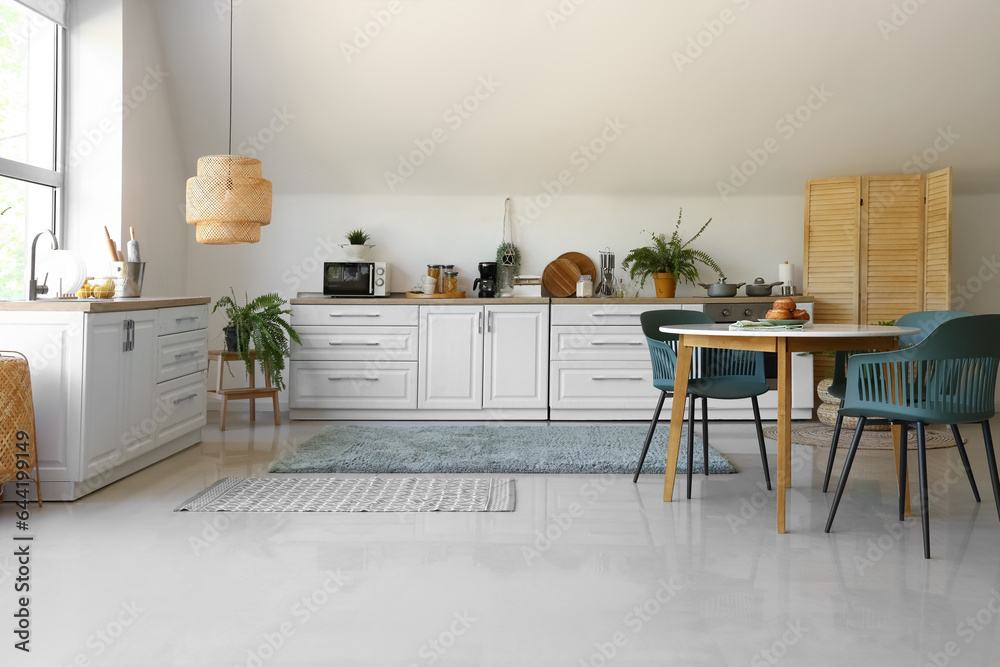 Interior of modern kitchen with white counters and dining table