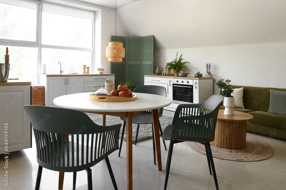 Dining table with cinnamon rolls, tea leaves and cups in modern kitchen