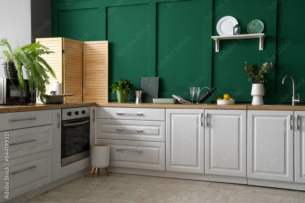 White counters with eucalyptus branches, wine bottle and utensils in modern kitchen