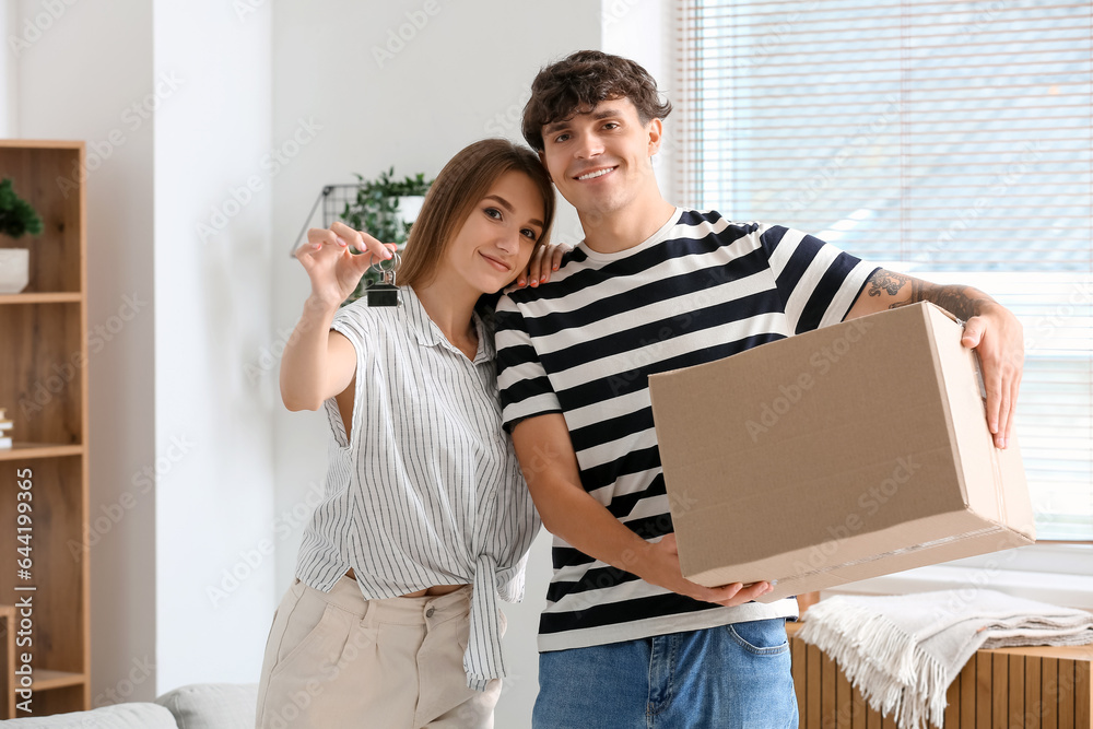 Young couple with keys and moving box in their new flat