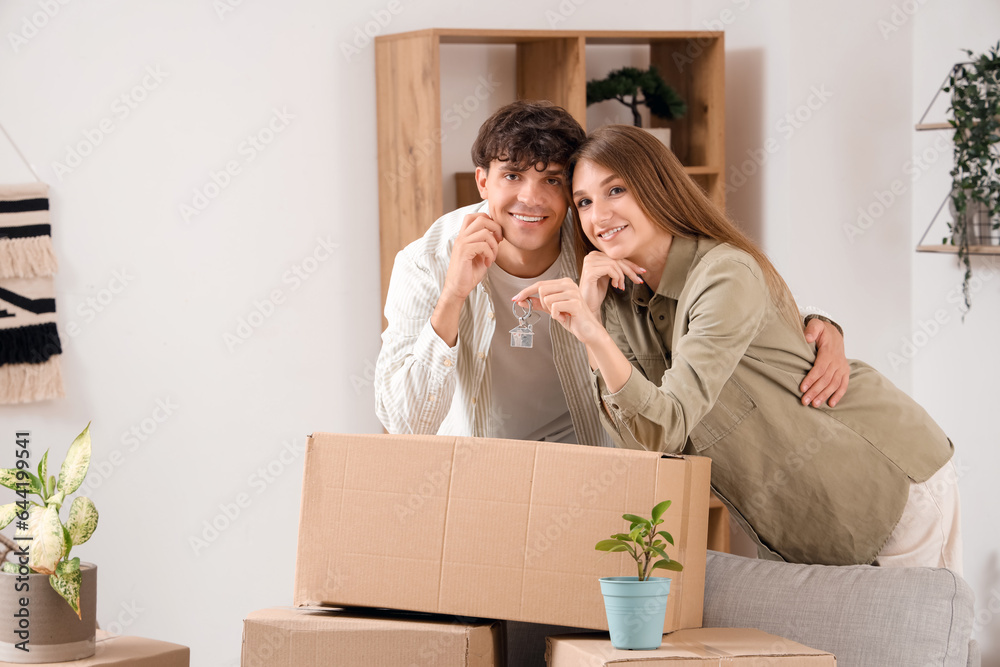 Young couple with keys and moving box in their new flat