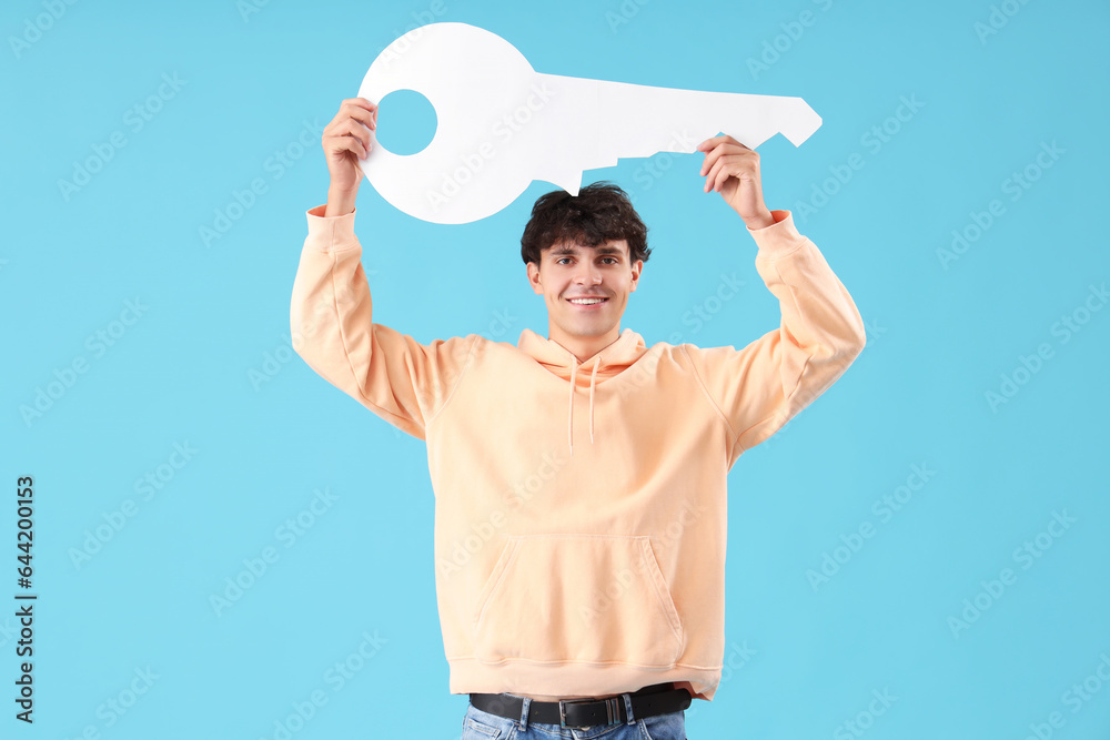 Young man with paper key on blue background