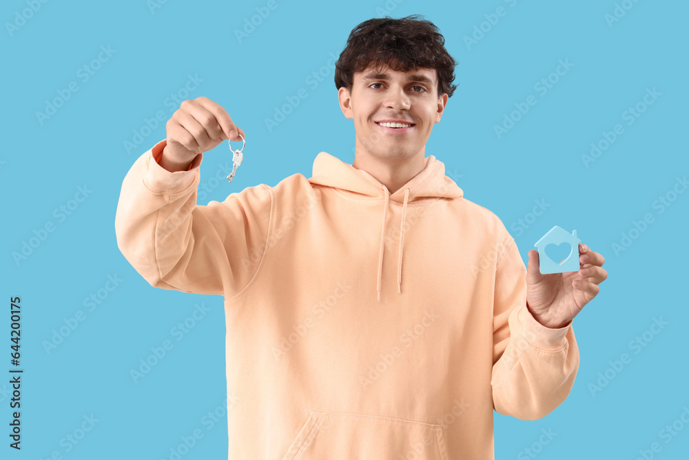 Young man with key and house figure on blue background