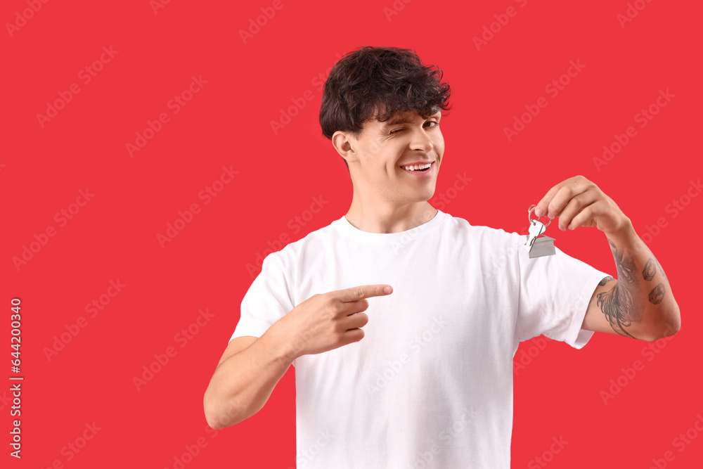 Young man pointing at keys from house on red background