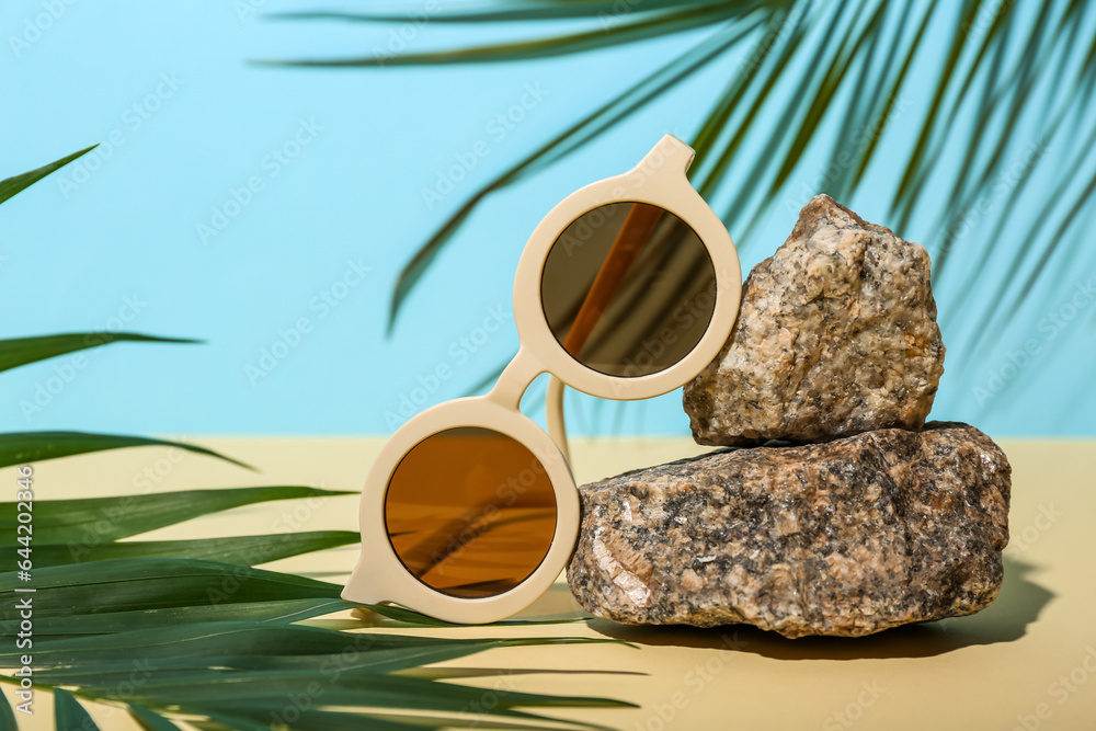 Stones with stylish sunglasses and palm leaves on yellow table