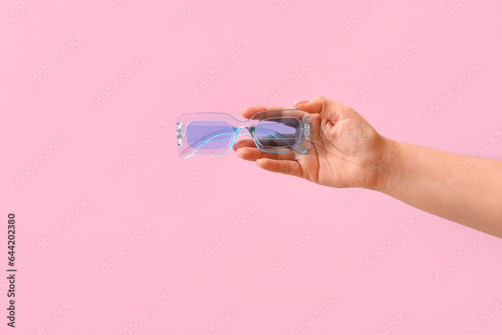 Woman holding stylish sunglasses on pink background