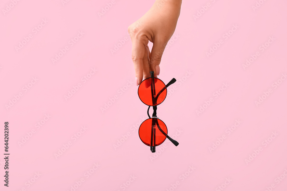 Woman holding stylish sunglasses on pink background