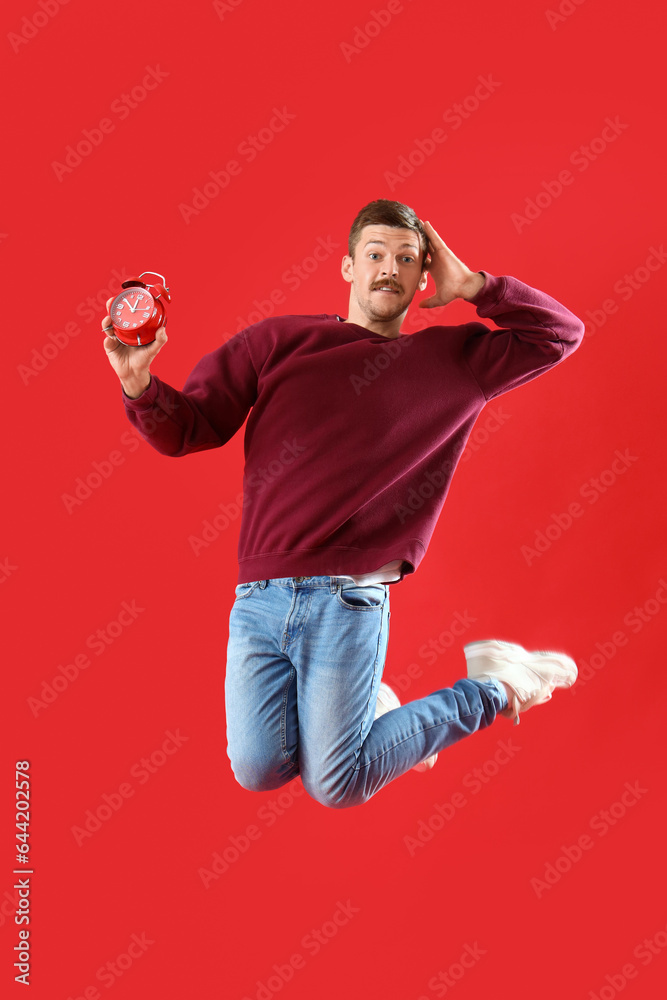 Worried jumping young man with clock on red background