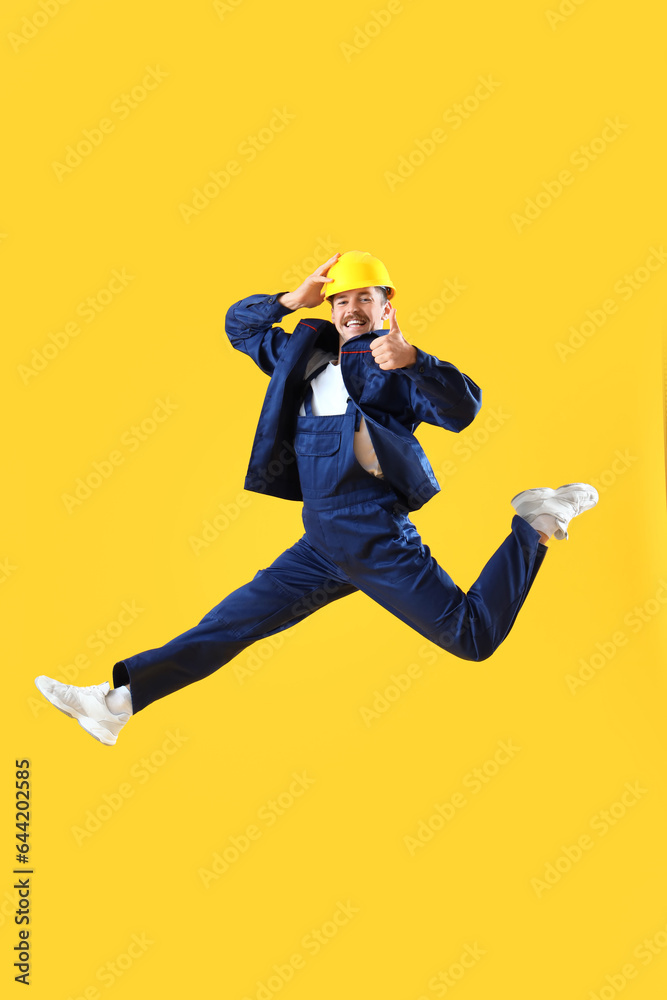 Jumping male worker showing thumb-up on yellow background