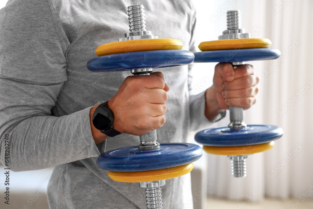 Sporty young man doing exercise with dumbbells at home, closeup