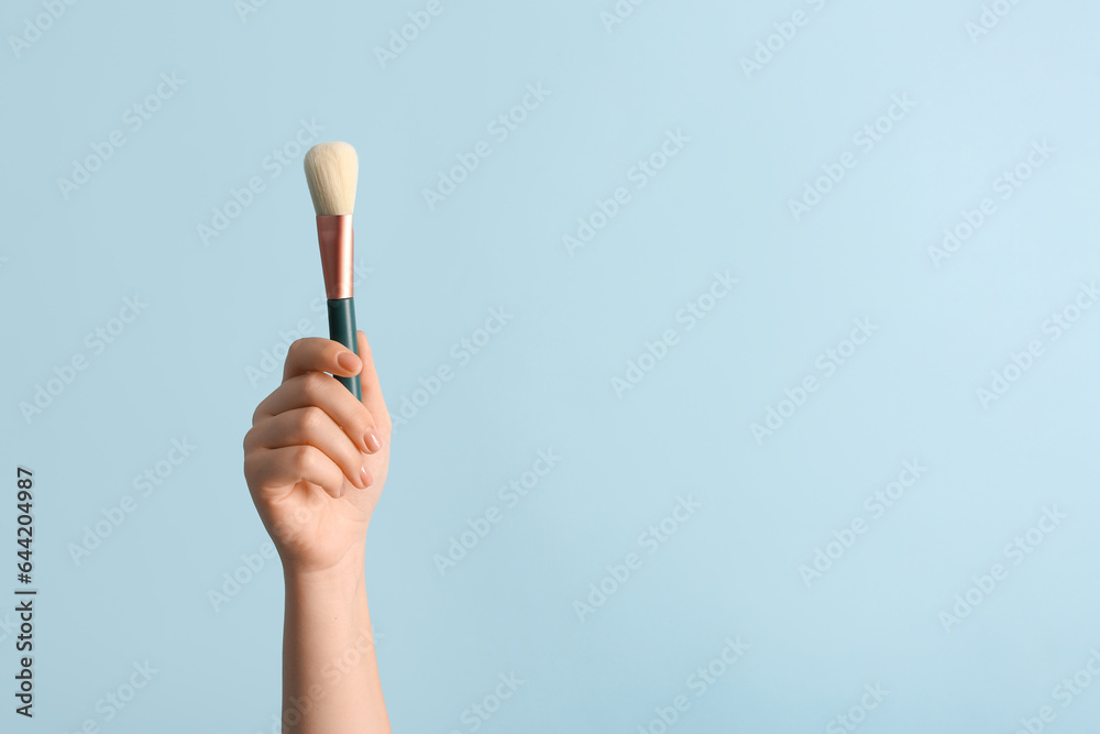 Female hand with makeup brush on blue background