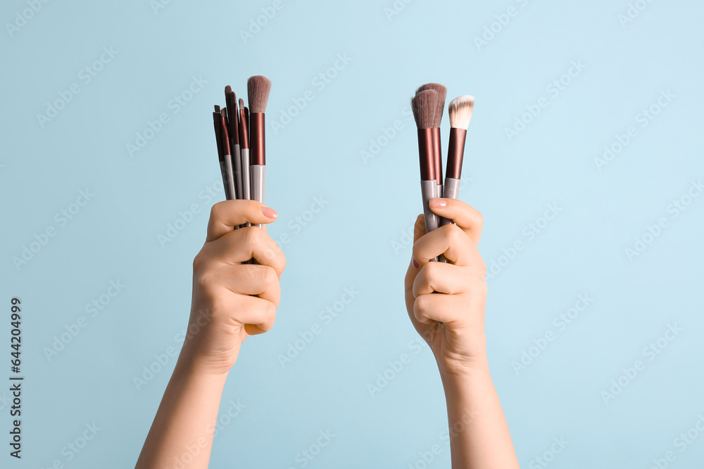 Female hands with makeup brushes on blue background