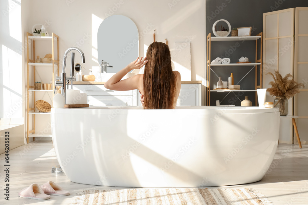 Young woman taking bath at home, back view