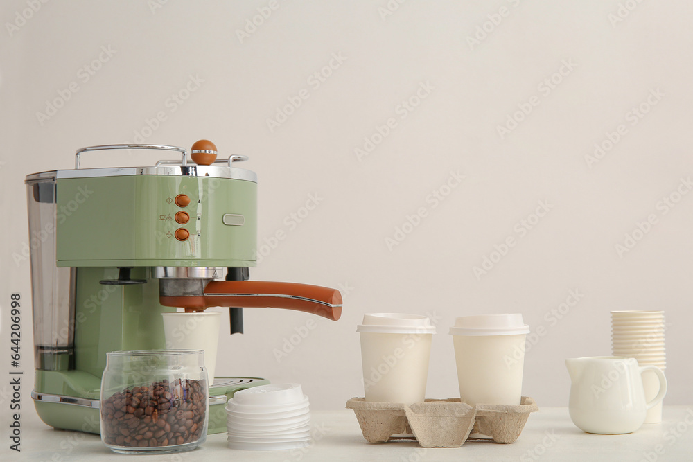 Modern coffee machine, takeaway cups, lids and beans on white background