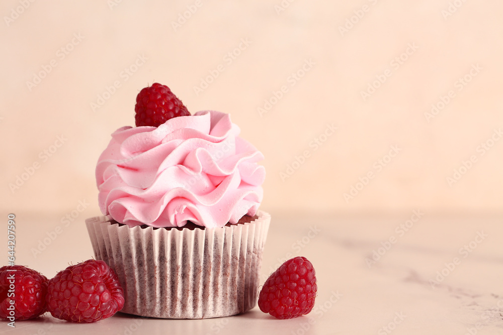 Tasty raspberry cupcake and fresh berries on beige background