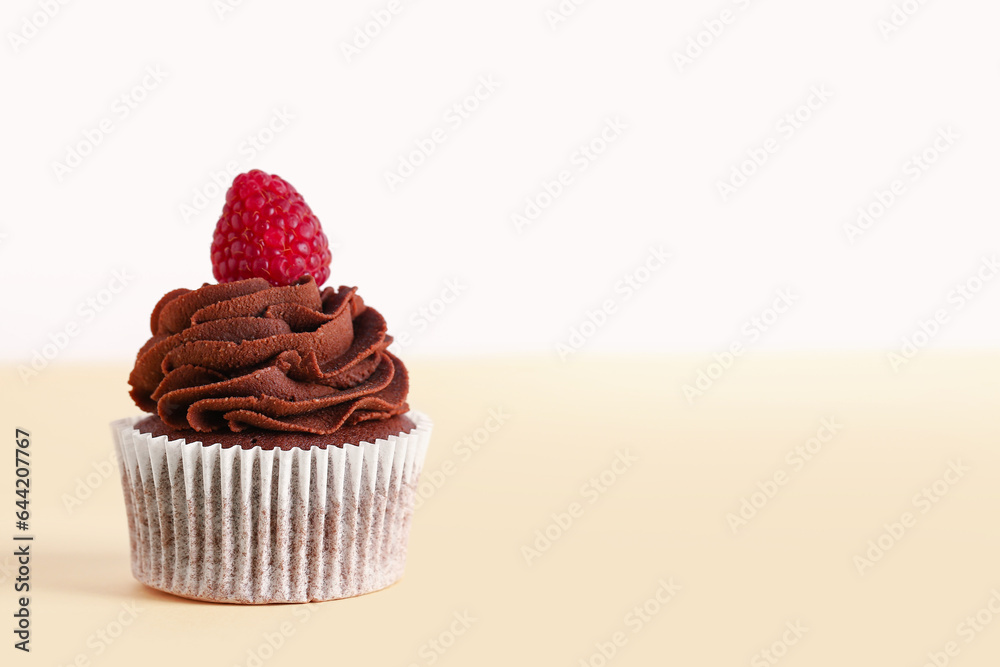 Tasty chocolate cupcake with raspberry on beige background