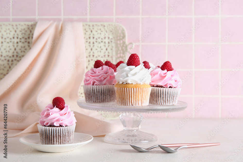 Stand and plate with tasty raspberry cupcakes on table