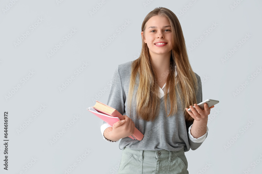 Happy female student with mobile phone, notebooks and book on grey background