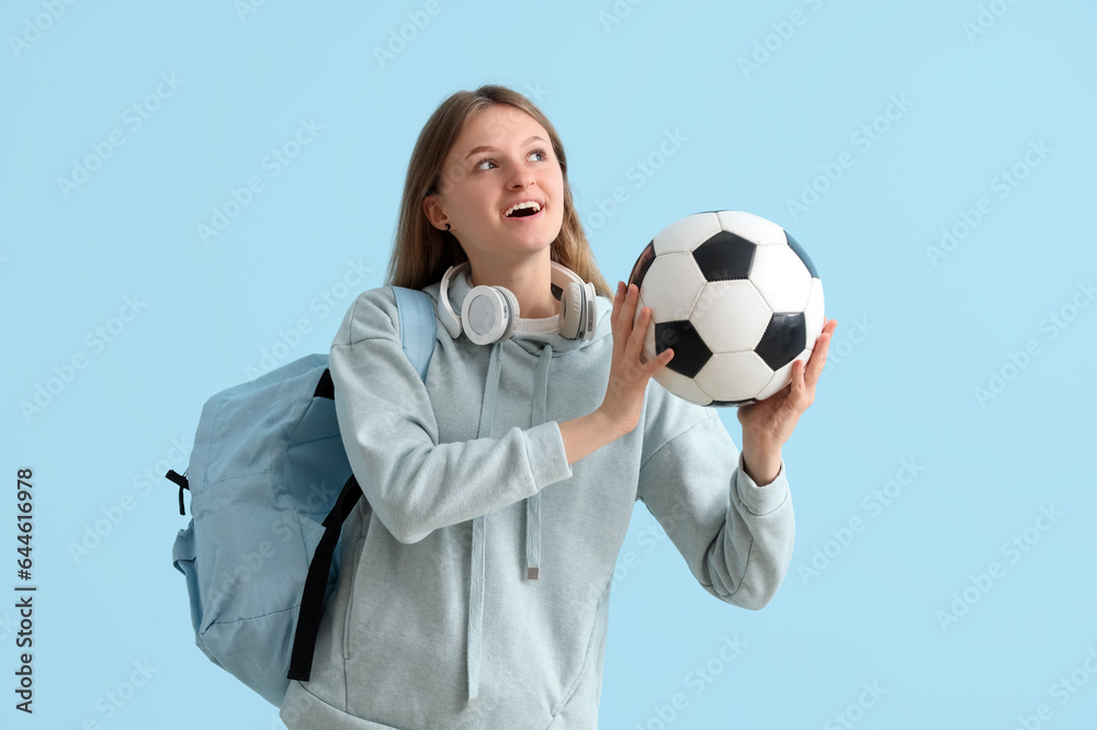 Female student with backpack, headphones and soccer ball on blue background