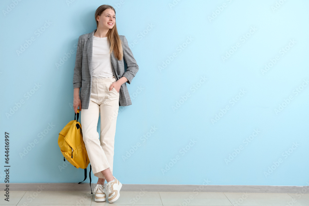 Female student with backpack near blue wall