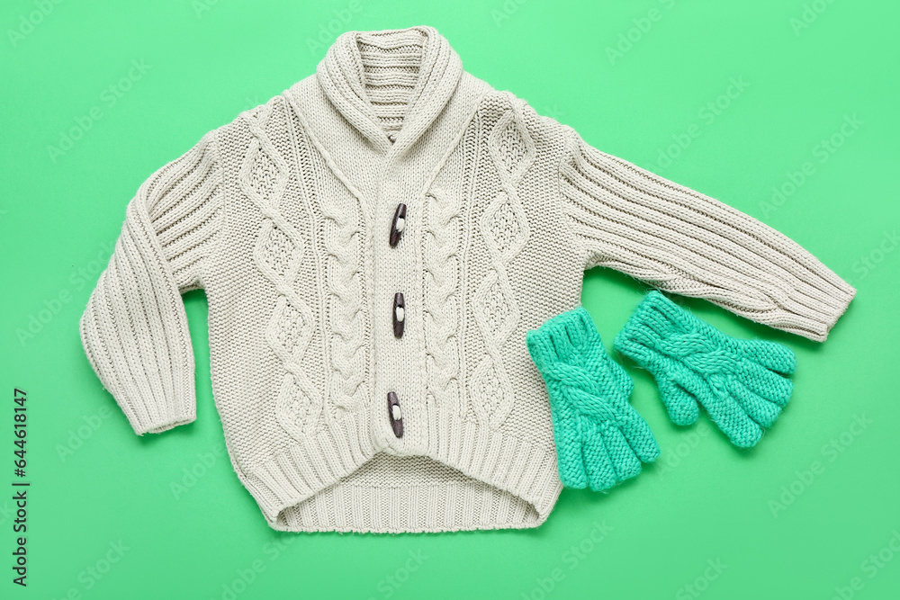 Childrens knitted sweater and warm gloves on color background