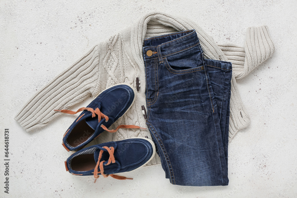 Stylish childrens jeans, sweater and shoes on light background