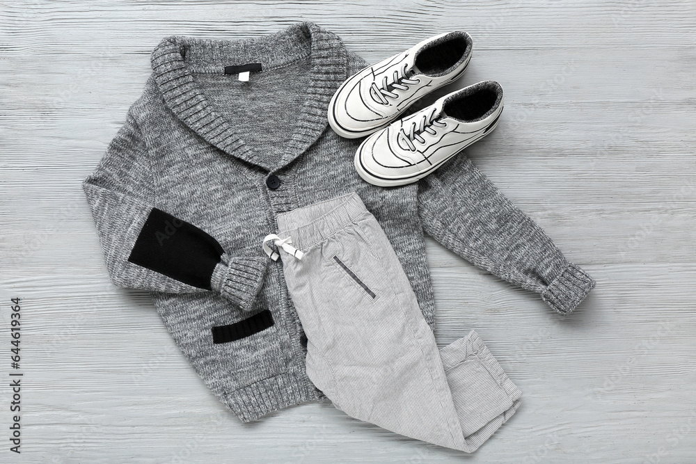 Stylish childrens sweater, pants and shoes on grey wooden background