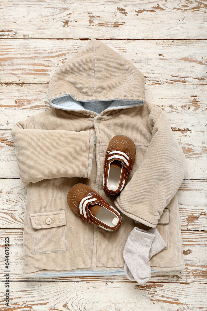 Stylish baby jacket, socks and booties on light wooden background