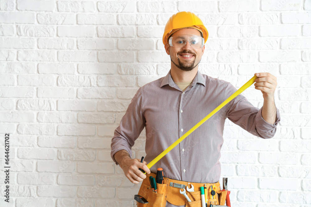 Male builder with tape measure near white brick wall