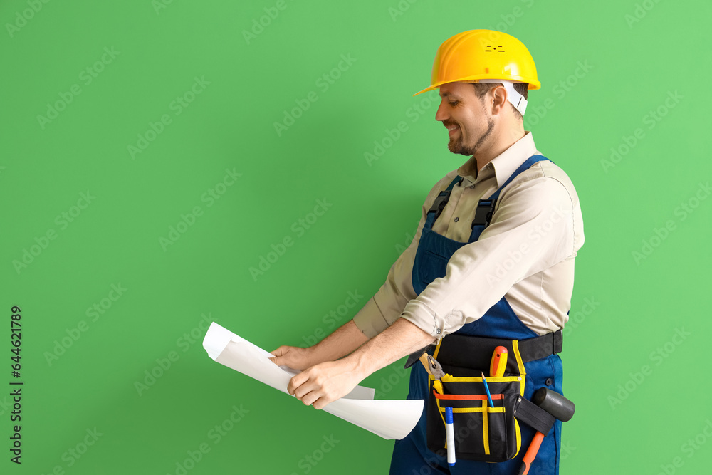 Male builder with house plan on green background