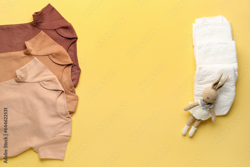 Set of baby bodysuits, toy and diapers on color background