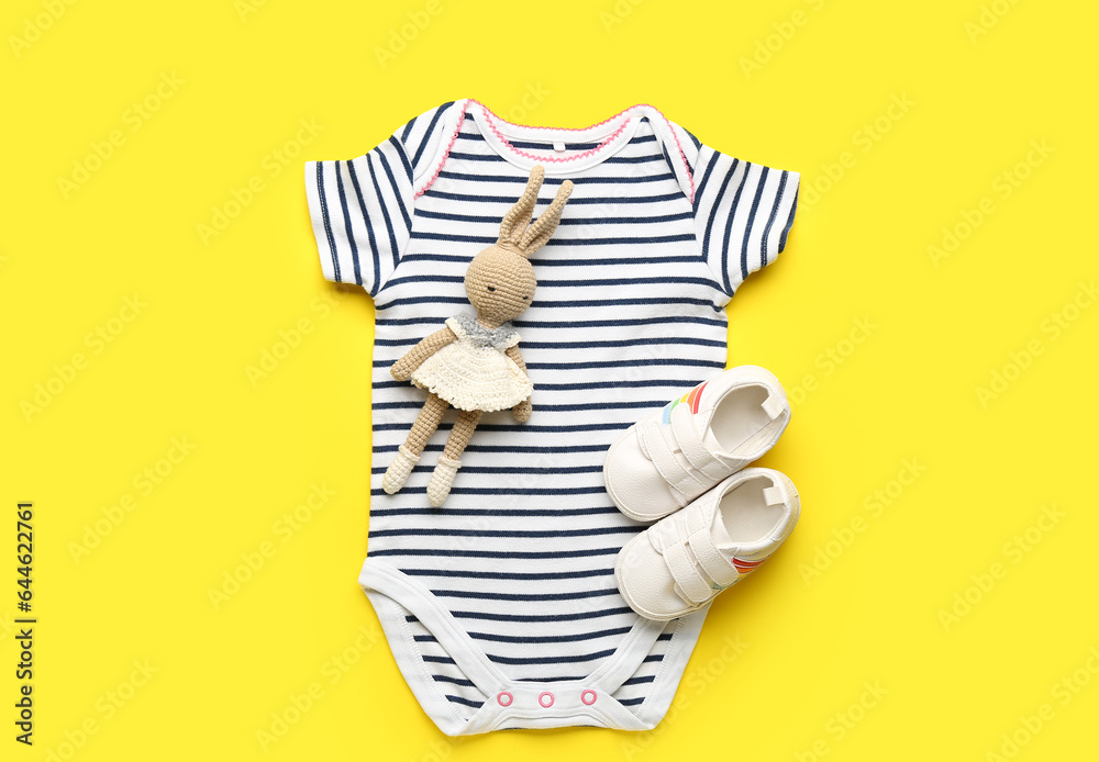 Baby bodysuit, booties and knitted toy on yellow background