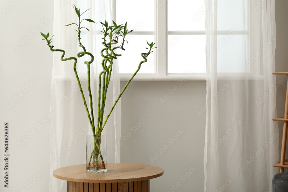 Vase with bamboo stems on table near window