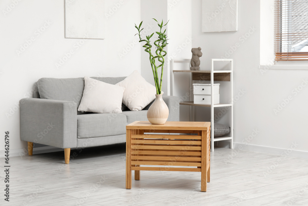 Vase with bamboo stems on wooden table in light living room