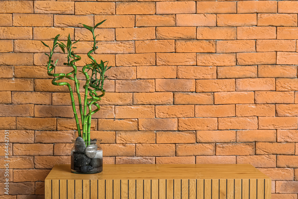 Vase with bamboo stems on table near brick wall