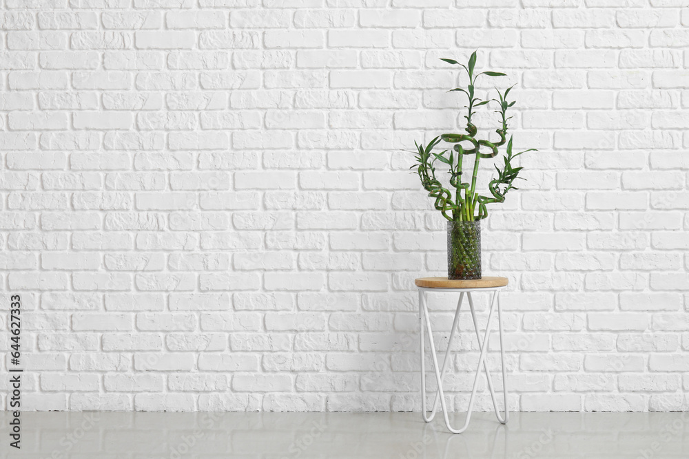 Vase with bamboo stems on table near white brick wall