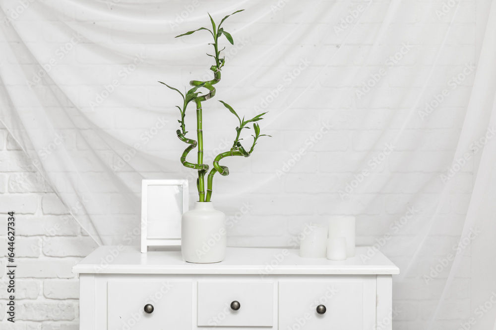 Vase with bamboo stems, candles and blank picture frame on table against white fabric background