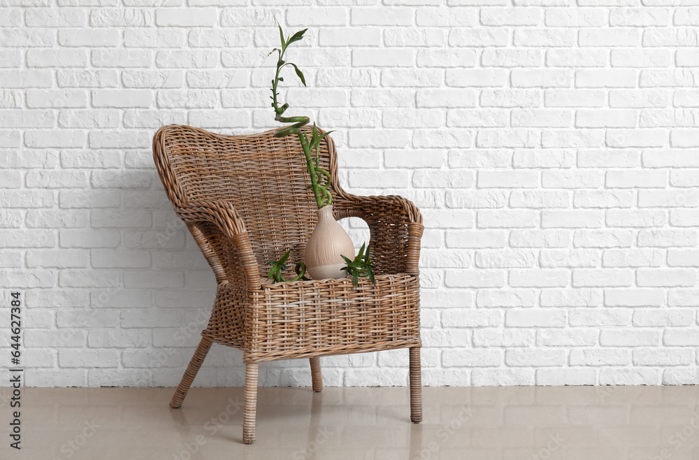 Vase with bamboo stems and rattan armchair near brick wall