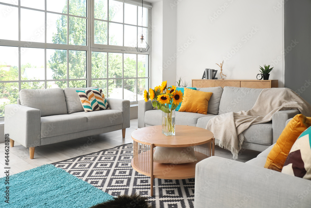 Cozy grey sofas and vase with beautiful sunflowers in interior of light living room