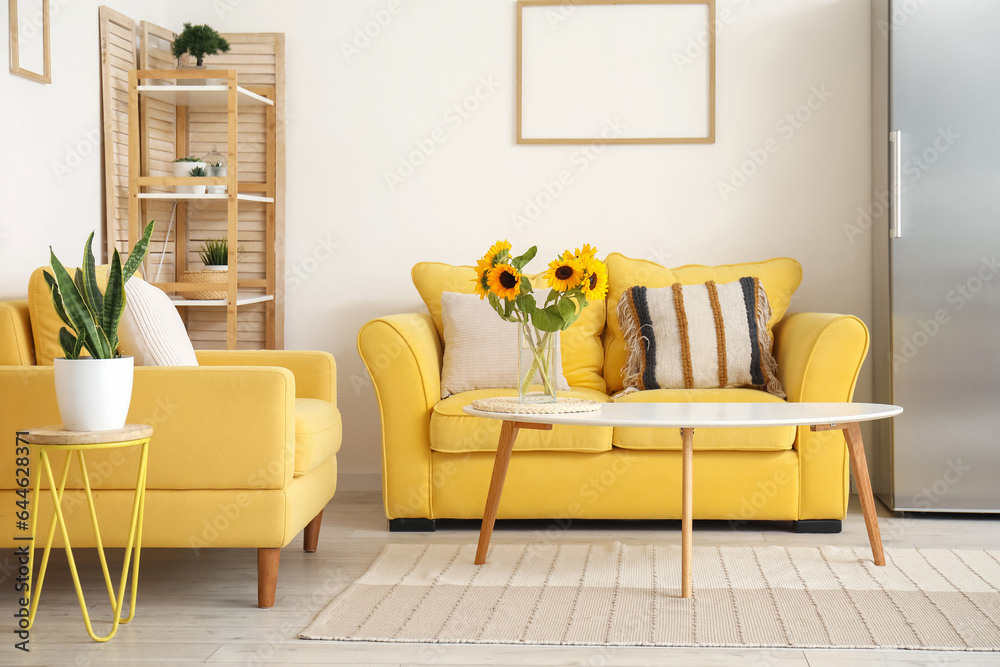 Vase with beautiful sunflowers, yellow sofa and armchair in interior of stylish living room