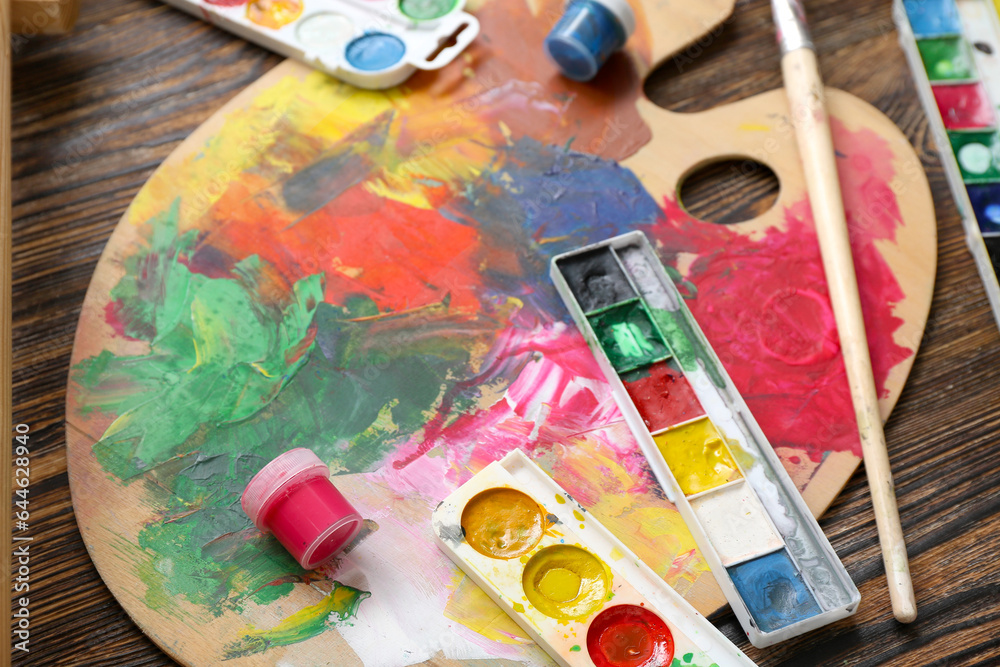 Palette with paints and brushes on wooden table