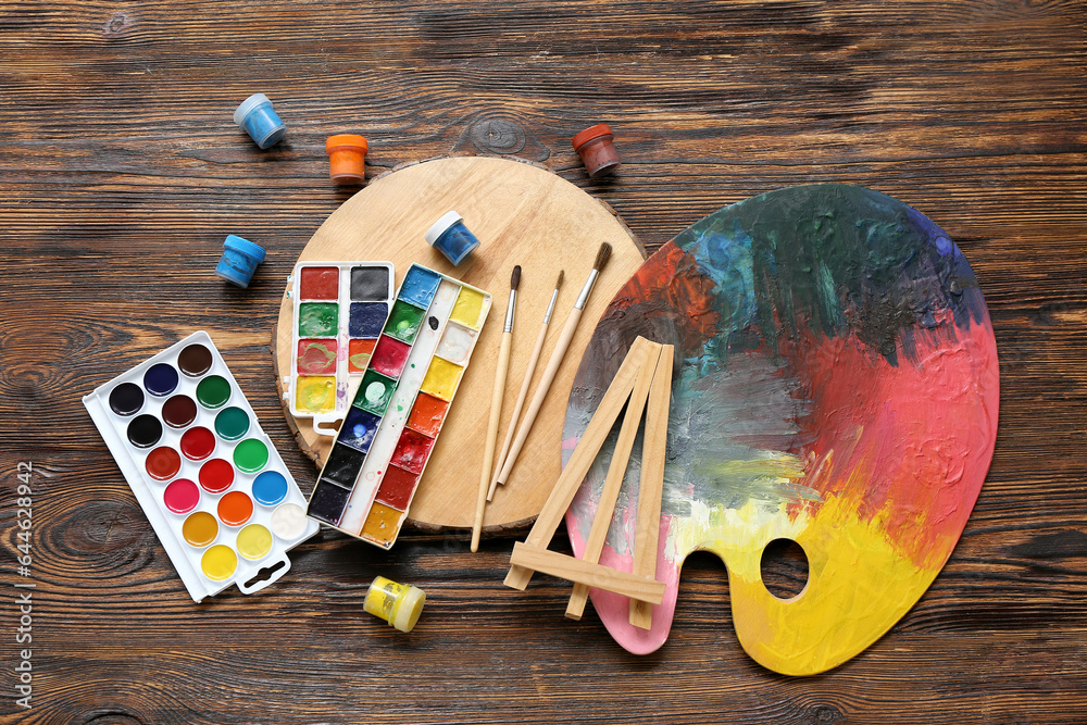 Palette with watercolor paints and brushes on wooden table