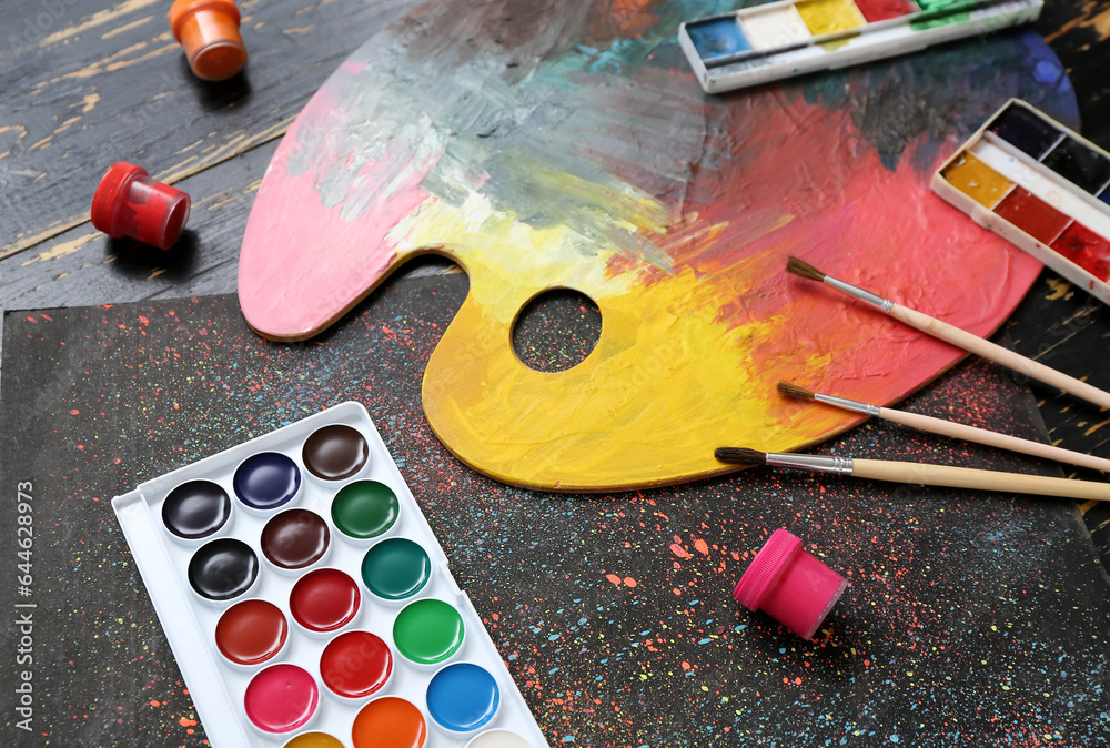 Palette with paints and brushes on black wooden table