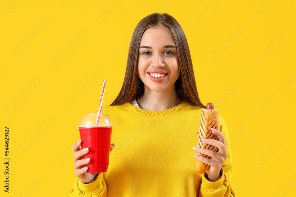 Young woman with french hot dog and soda on yellow background