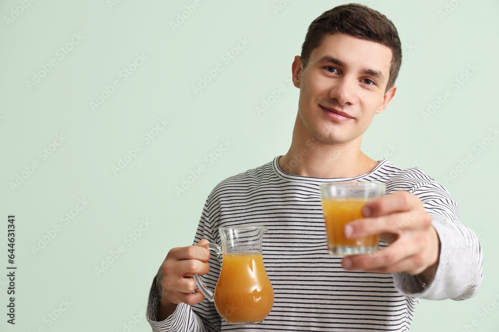 Young man with jug and glass of juice on green background