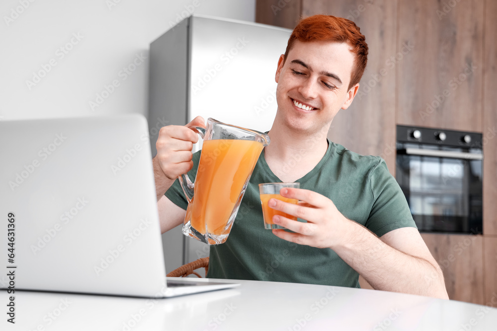 Young man with jug and glass of juice in kitchen