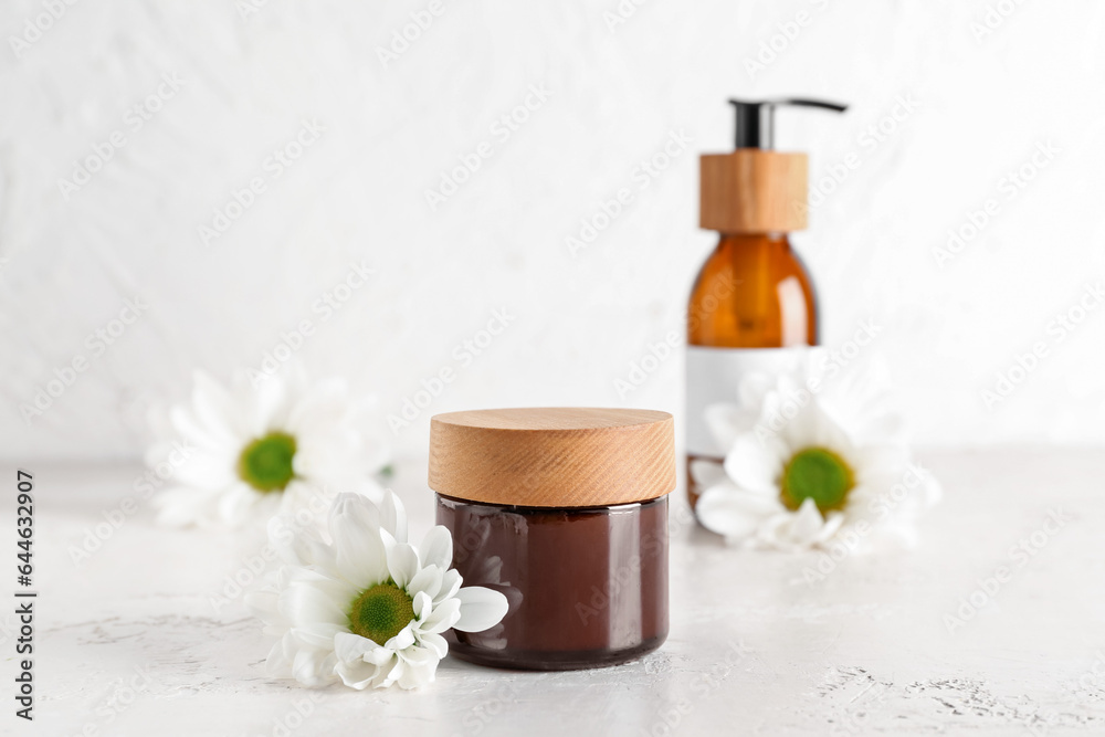 Jar of cosmetic product and chamomile flowers on light background